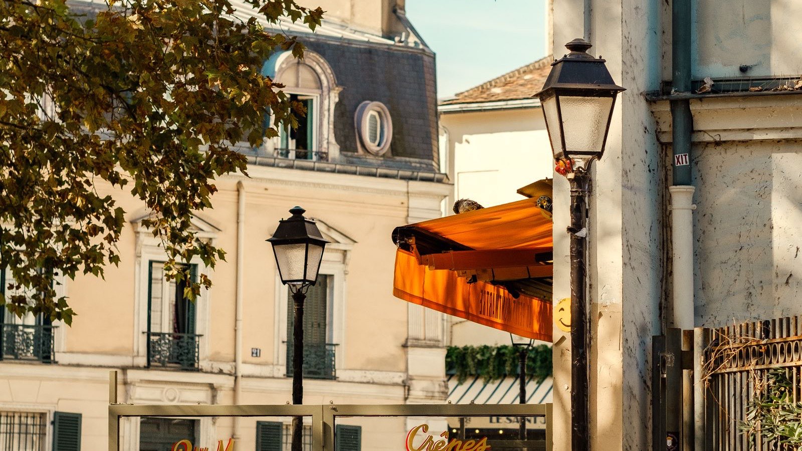 A Paris street corner in Montmartre with lampposts, an orange cafe awning, and warm afternoon light